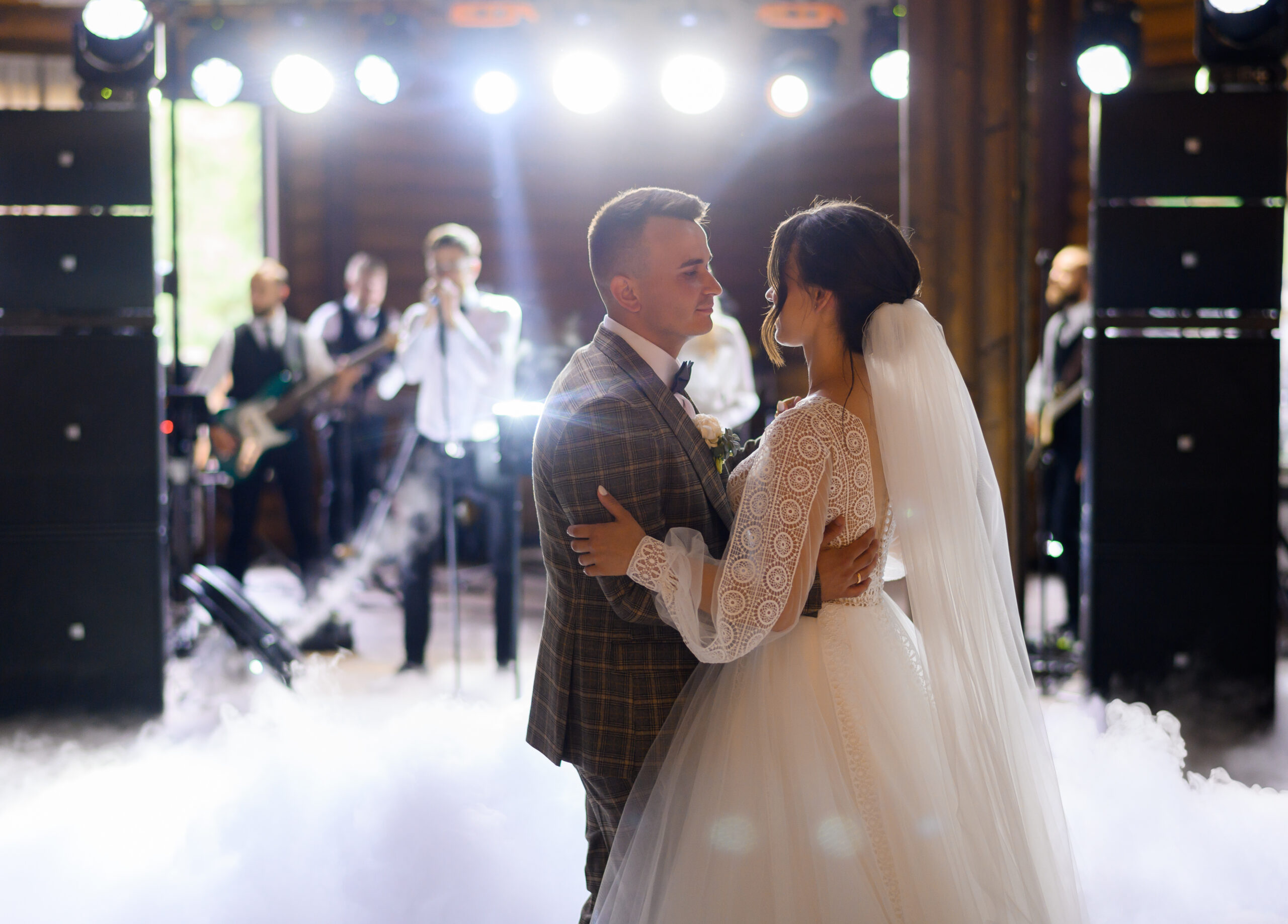 Blur of faceless musician standing and singing song with band while newlyweds, dancing first wedding dance in centre of hall among smoke effects